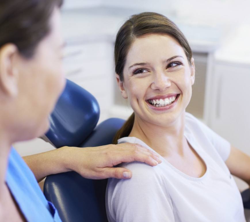 Woman smiling as dental team member puts their hand on her shoulder